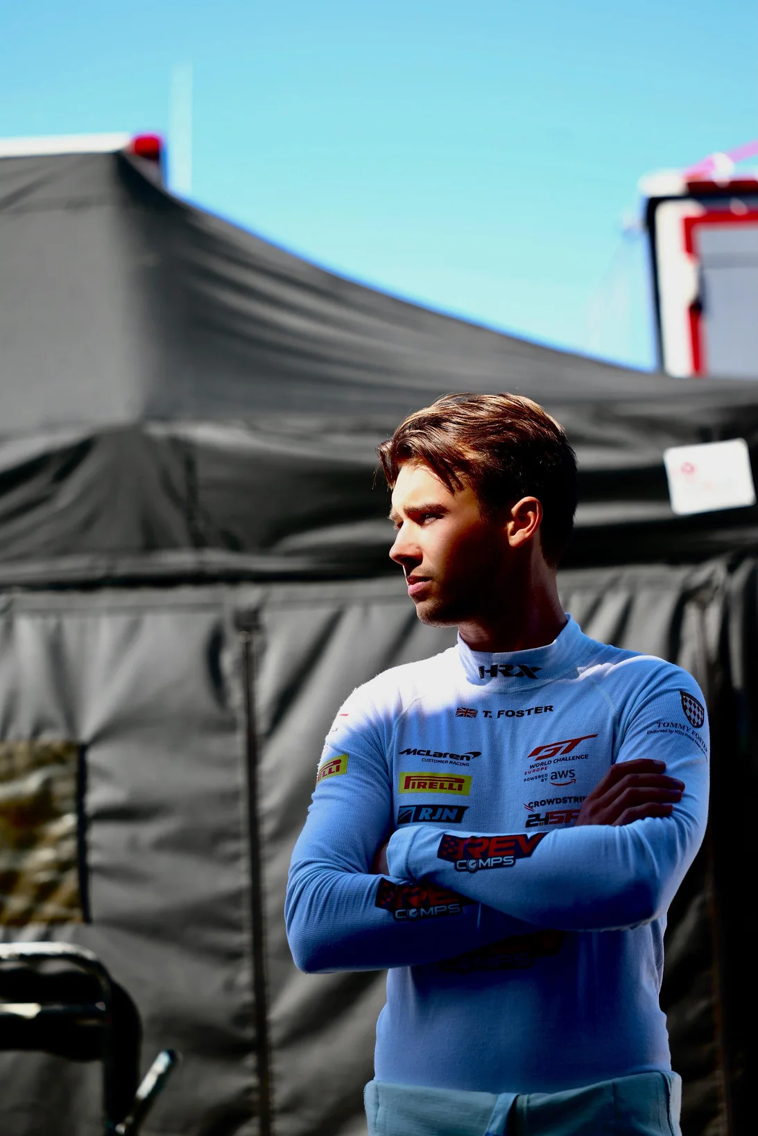 Racing driver Tommy Foster in his race suit, arms folded, in the paddock